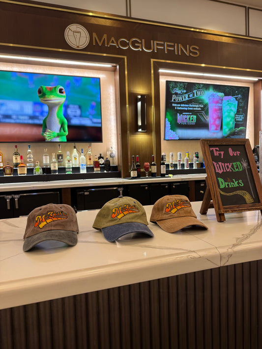 Three branded caps on a bar counter with a 'MacGuffins' sign and digital screens in the background.