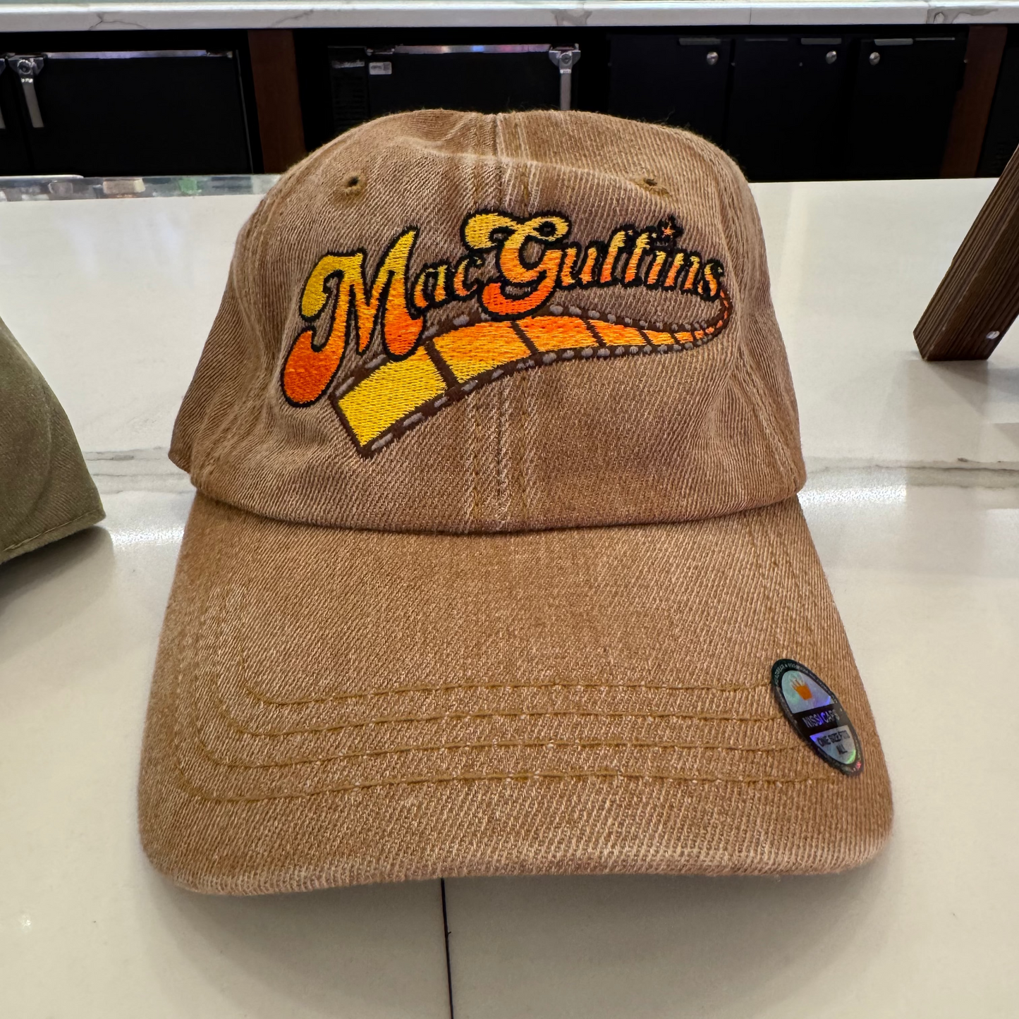 Brown cap with 'MacGuffins' logo on a counter